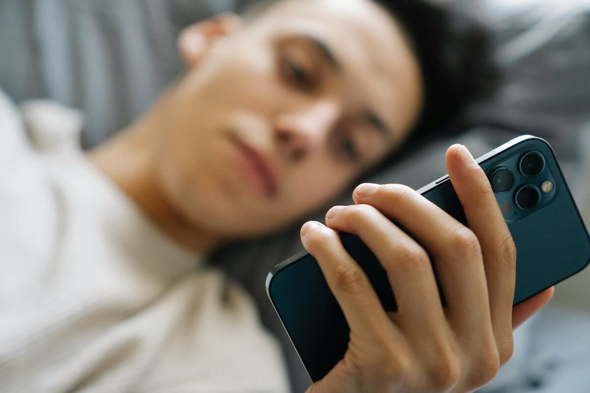 man holding phone in bed by eren li